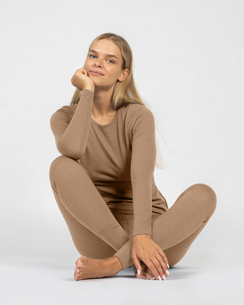 Person wearing a beige merino base layer outfit sitting on a white background