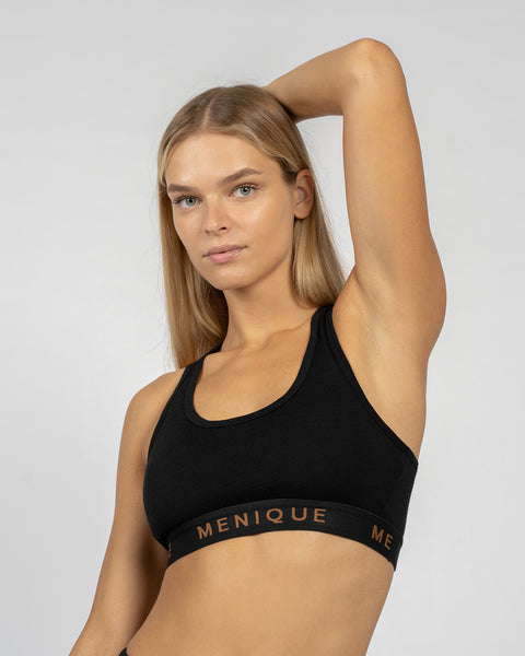 Vrouw draagt een zwarte sportbeha van merinowol met racerback-ontwerp, poseert met één arm omhoog.