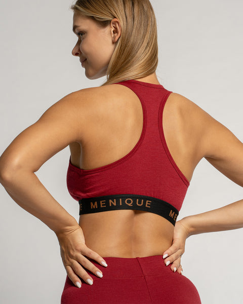 Vrouw draagt een rode sportbeha en legging met 'Menique' merknaam op een lichtgrijze achtergrond