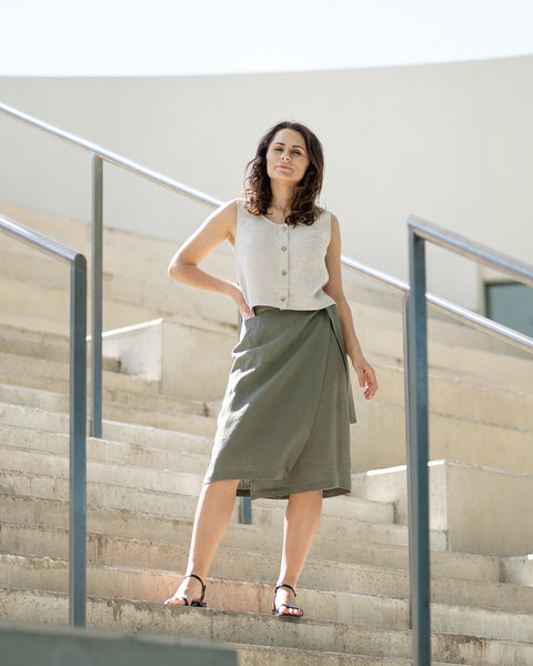 Woman standing on a set of stairs wearing a sleeveless menique linen top in the color natural and linen skirt.