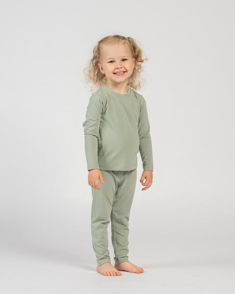Happy child standing in green bamboo long-sleeve top and bottoms, barefoot.