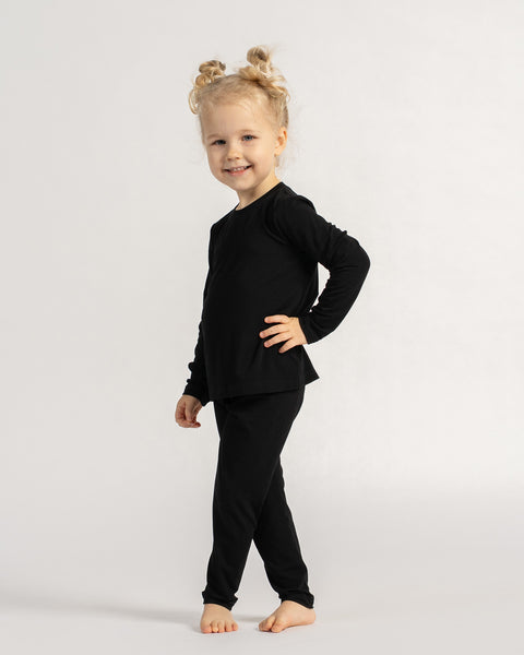 Kind staat in een zwart bamboe shirt met lange mouwen en legging, toont een soepele pasvorm en dagelijks draagcomfort.