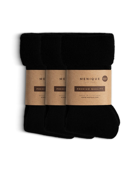 Set van drie paar zwarte herensokken van sherpa fleece, opgerold en verpakt in Menique bruin papier met het etiket ‘Premium Kwaliteit – Merinowol’.