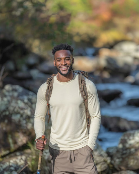 Man with a backpack and hiking stick standing by a river with a natural background