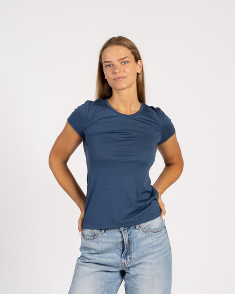 A woman standing facing forward in a blue t-shirt and jeans, with both hands on her hips.
