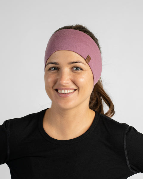A front-facing studio portrait of a woman smiling warmly, wearing a mauve knit headband and a black crewneck top.