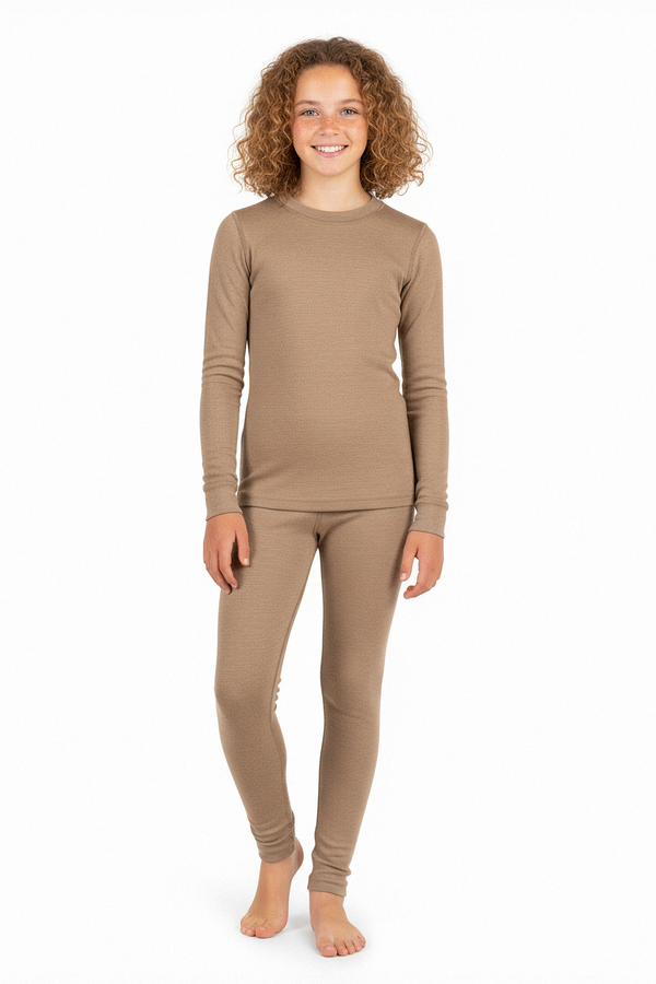 Een meisje draagt een beige merinowollen ondershirt met lange mouwen en bijpassende legging, staat blootsvoets en glimlacht tegen een witte studioachtergrond.