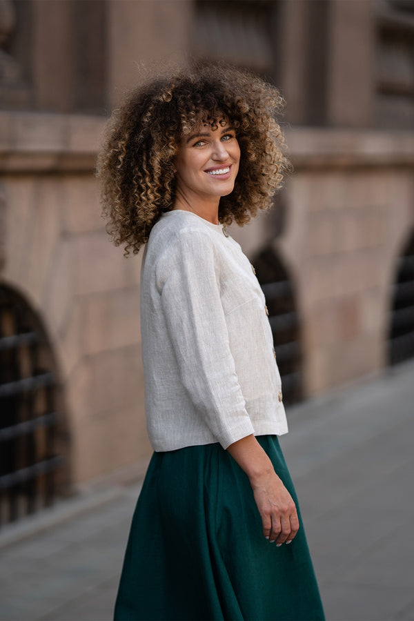 Een model draagt een natuurlijk beige linnen jasje Alice met knopen, met een losse pasvorm, driekwartmouwen en een minimalistisch ontwerp