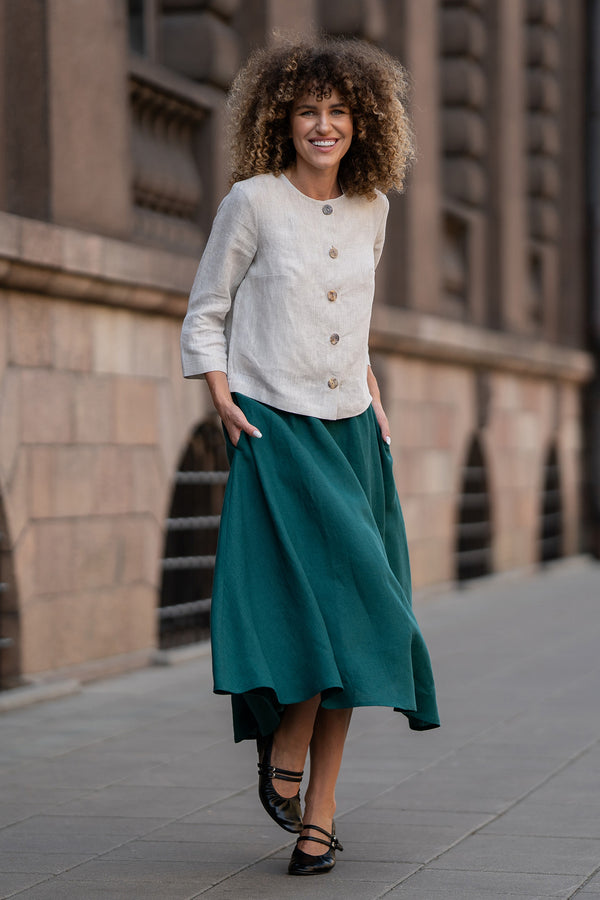 A model wearing a natural beige linen jacket Alice with buttons, featuring a relaxed fit, 3/4-length sleeves, and a minimalist design. The jacket is paired with matching dark green skirt