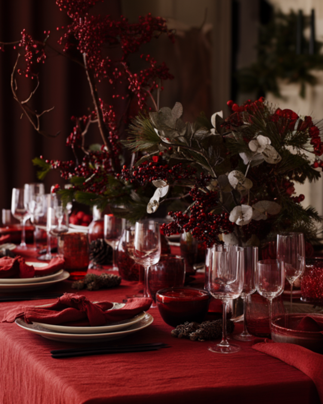 Decoratieve tafelaankleding met rood tafelkleed, glazen en bloemstukken.