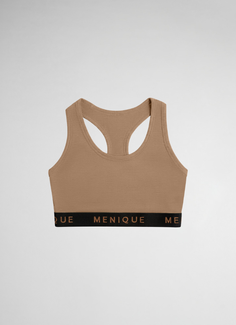 A tan racerback sports bra is presented flat against a seamless, light grey backdrop. The bottom of the bra includes a wide black elastic band with the brand name "MENIQUE" prominently displayed in brown lettering.