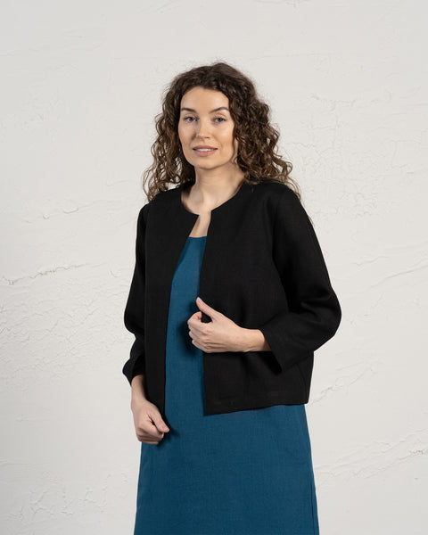Woman wearing a black jacket over a blue dress against a white background