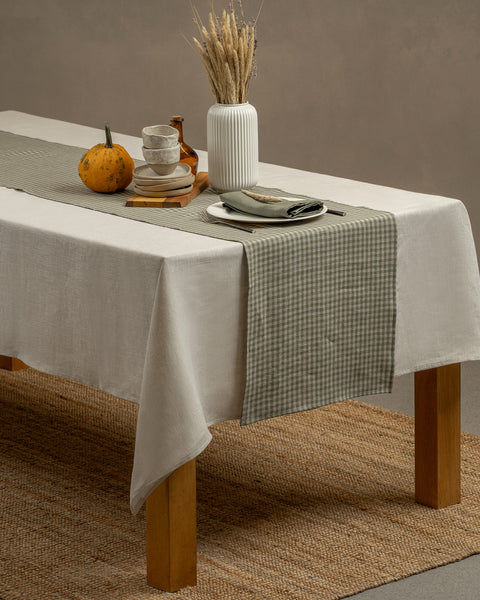 The green check linen table runner on top of a wooden table, captured in a close up picture from the corner of the table. 
