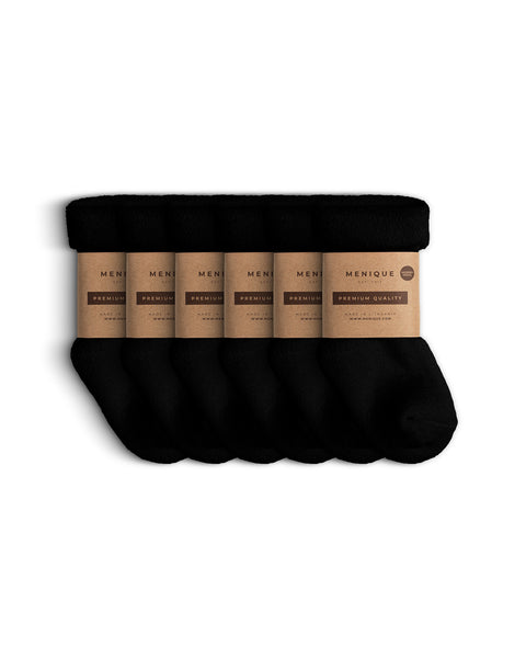 Six pairs of soft black sherpa fleece socks for children, arranged side by side with Menique brown paper packaging labeled ‘Premium Quality.