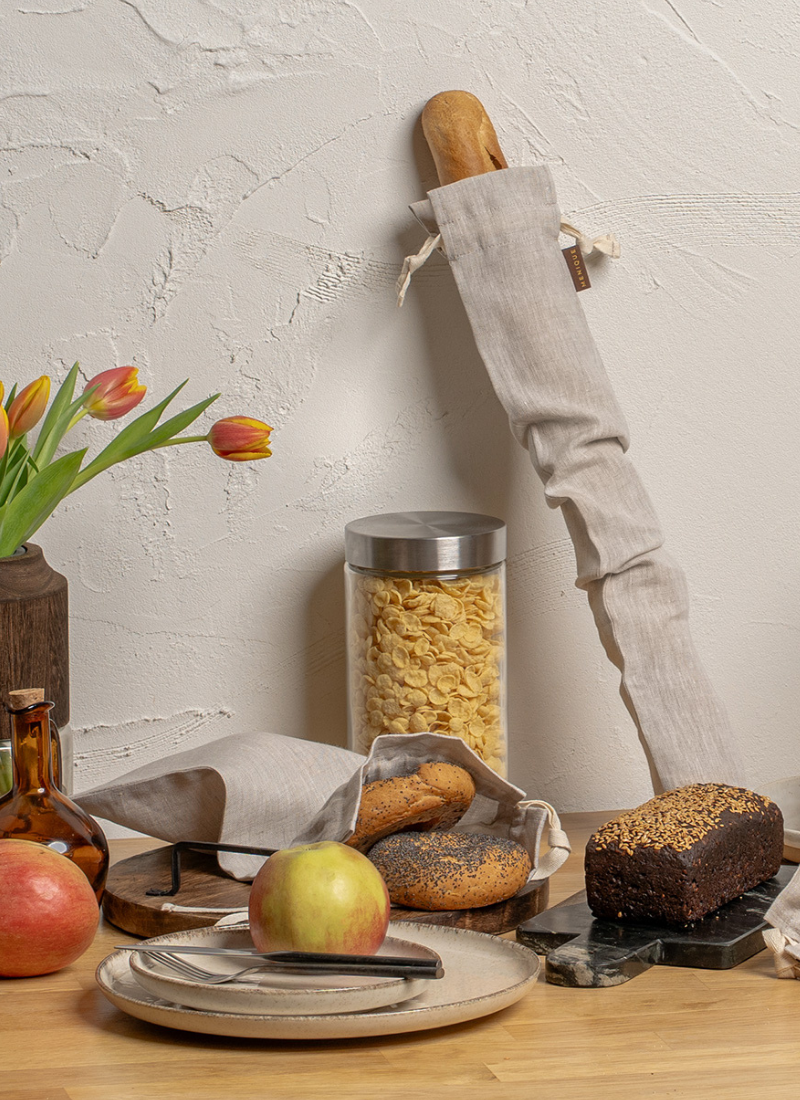 Linen bread bag and fresh baked goods on kitchen counter with apples and glass jar