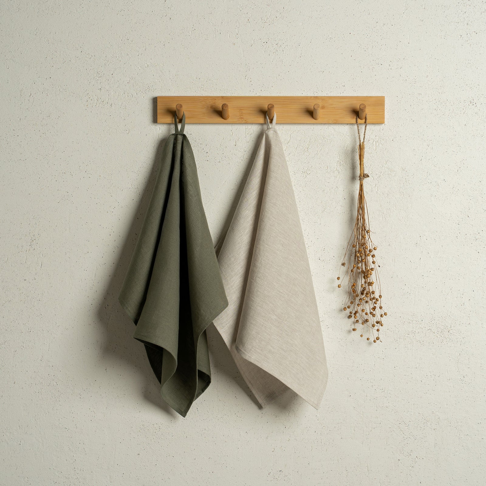 Twee menique linnen keukendoeken hangen aan een houten rek aan de muur. De kleuren van de doeken zijn steengroen en groen geruit.