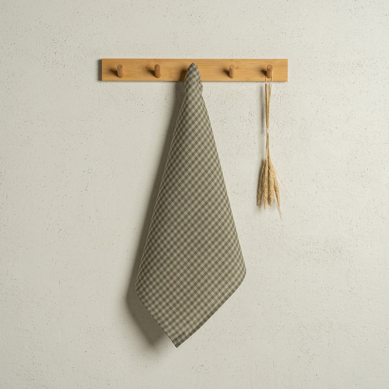 De menique vierkante linnen theedoek in de kleur donkergroen hangt aan een houten rek aan de muur.