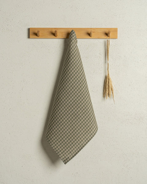 The menique square linen dish towel in color green check hanging on a wooden rack on a wall.