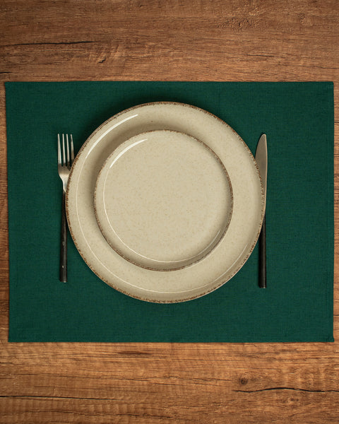 The menique linen placemat in dark green color on a wooden table top. 