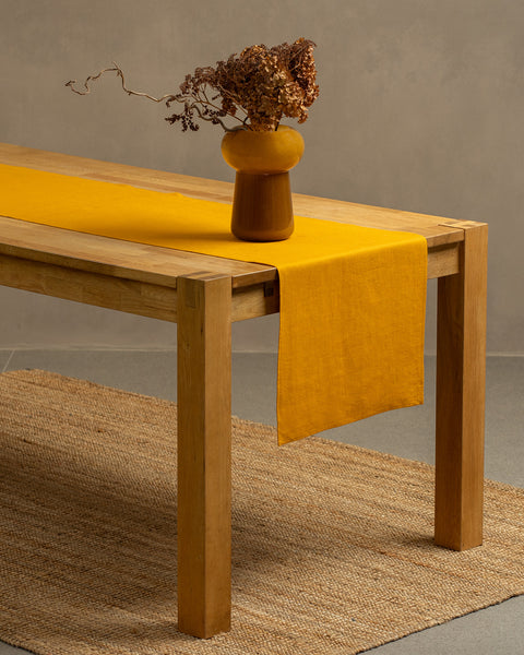 The menique spicy yellow color linen table runner on top of a wooden table. There is a vase on top of the runner.