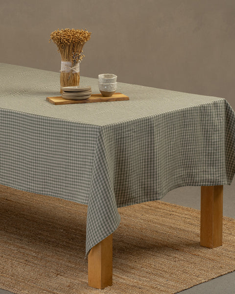 Het menique linnen tafellaken in groen geruit, dat over een houten tafel hangt, met een vaas, een houten plank en een set dessertborden met kleine klei schaaltjes erop.