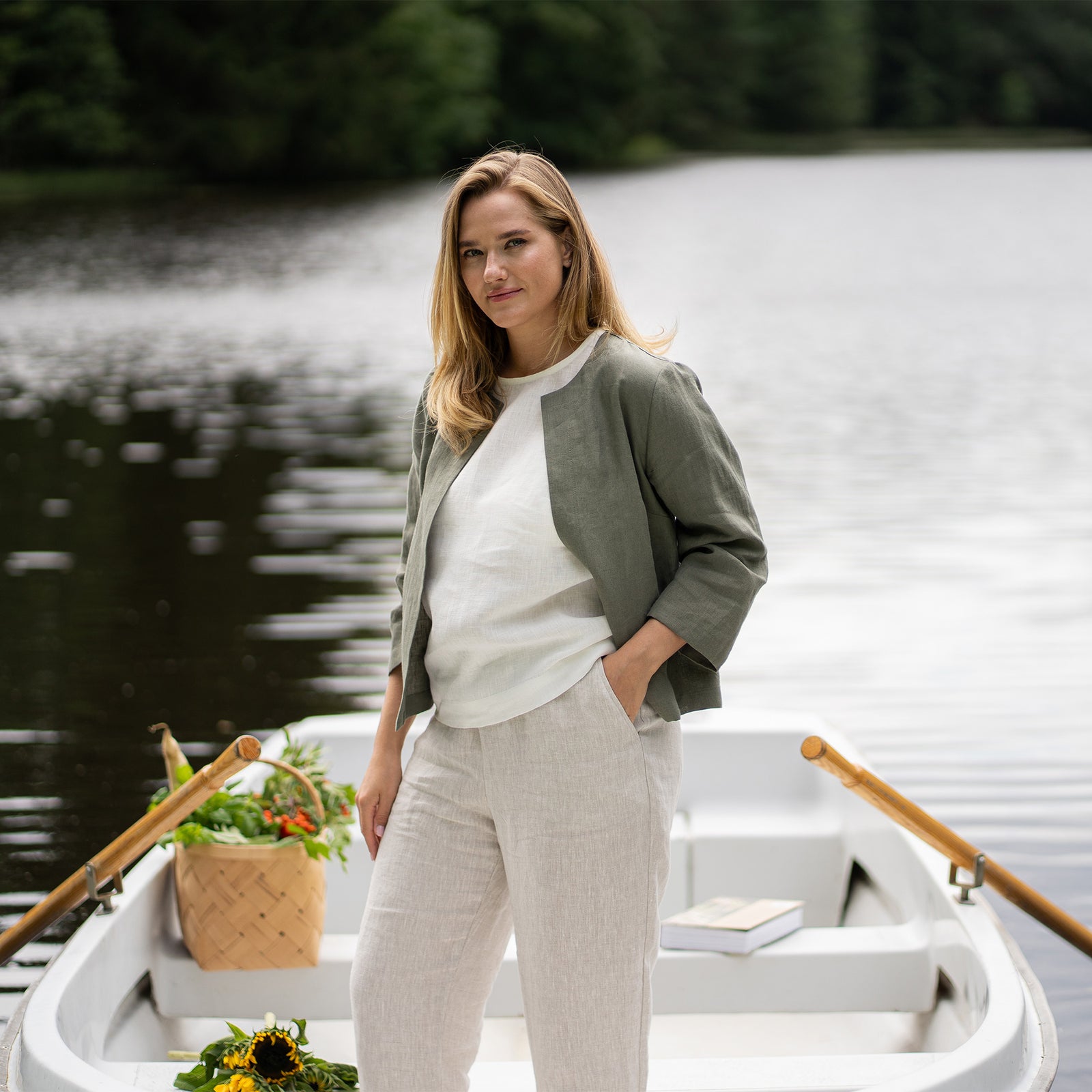 Vrouw draagt een natuurlijk linnen jasje en broek met een blauw shirt tegen een effen achtergrond