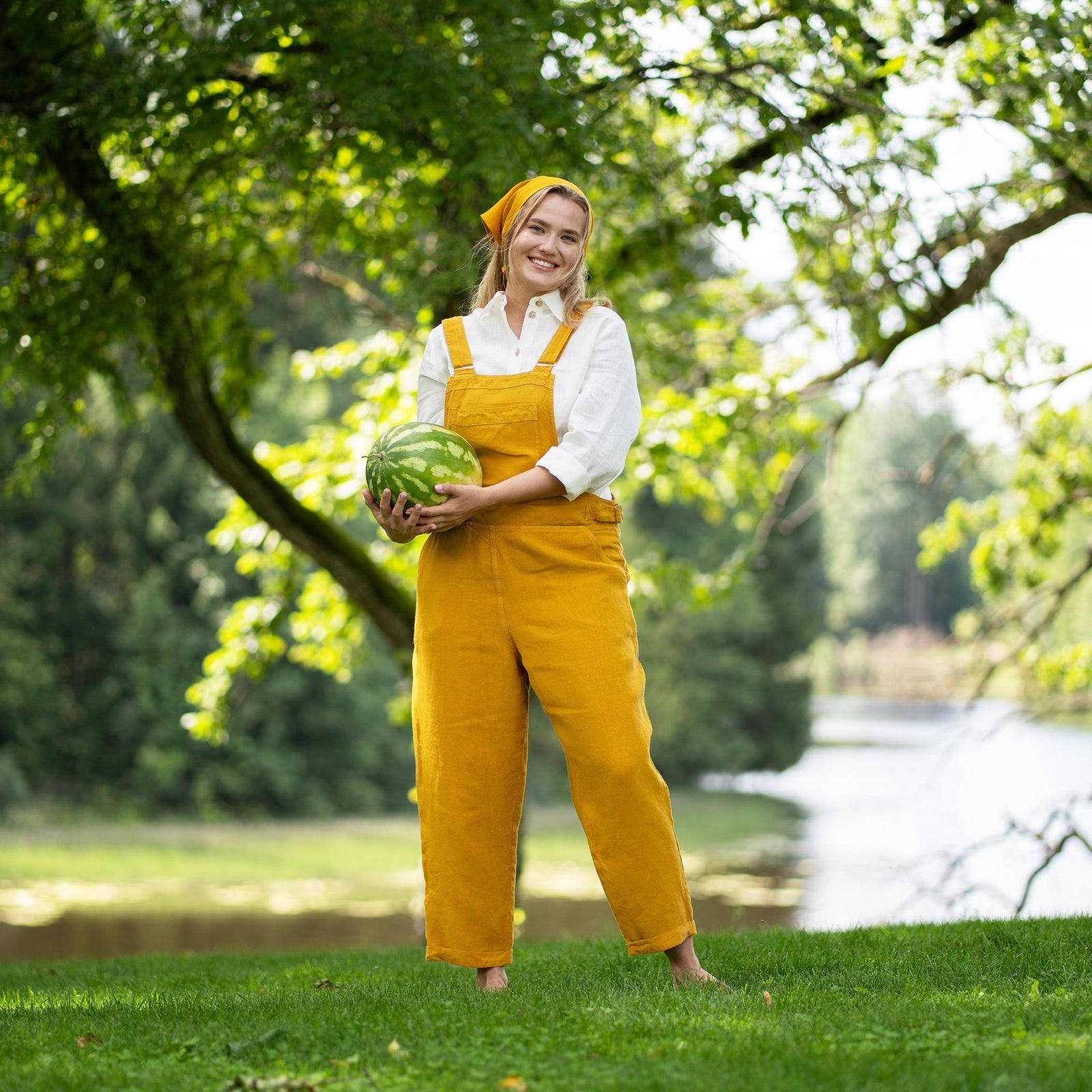 Vrouw in gele Nicci linnen jumpsuit die een stuk watermeloen vasthoudt in een parkachtige omgeving