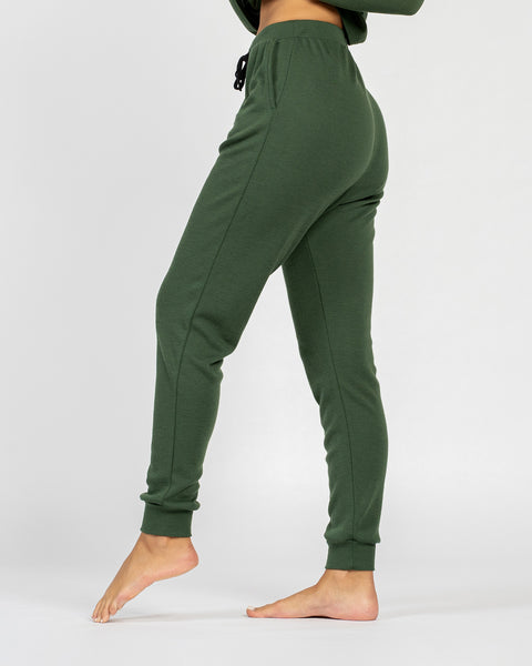 The menique women's merino wool 250gsm jogger sweatpants in dark green color. They have slightly elastic cuffs by the ankles and an elastic waist. There are visible side pockets.