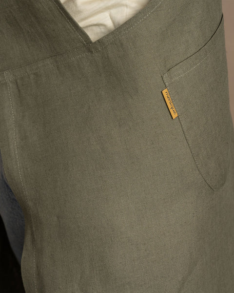 Een close-up van de gestructureerde linnenstof en het zakdetail van een stenen groene menique schort.