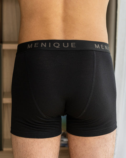 Een man draagt korte boxershorts gemaakt van merinowol, in de kleur zwart. De achterkant van de boxershorts is zichtbaar op de foto.