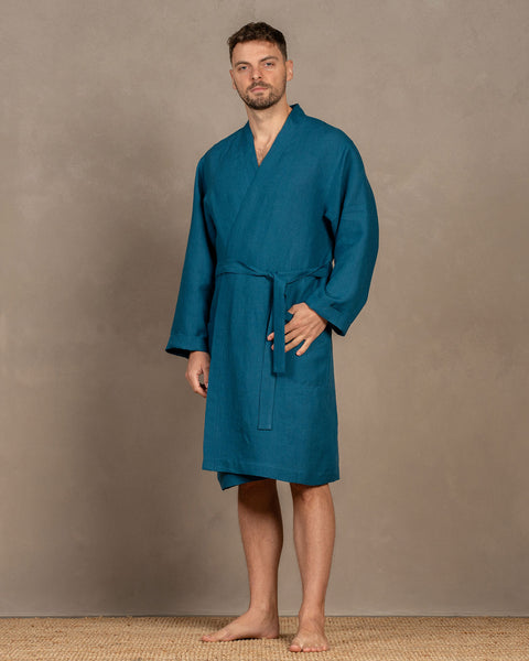 A man wearing the cobalt blue menique linen bathrobe. The bathrobe has pockets on the sides and a tie at the front.