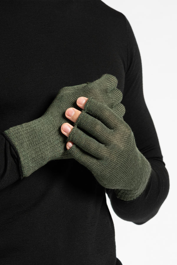 A person wearing a black long-sleeved shirt is shown from the chest up, putting on dark green fingerless gloves. The background is white.