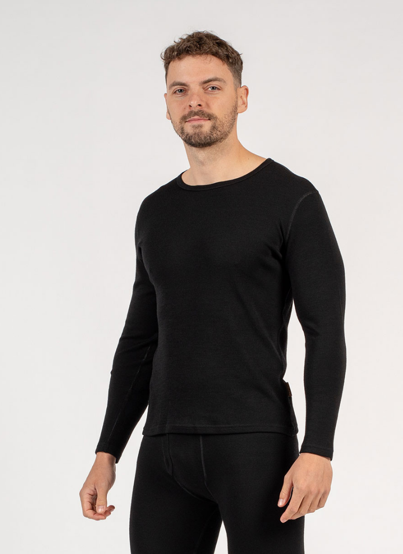 A man with a short beard stands facing forward in a black long-sleeve mid-layer top and black thermal leggings. The image is a clear studio shot set against a clean, light gray background.