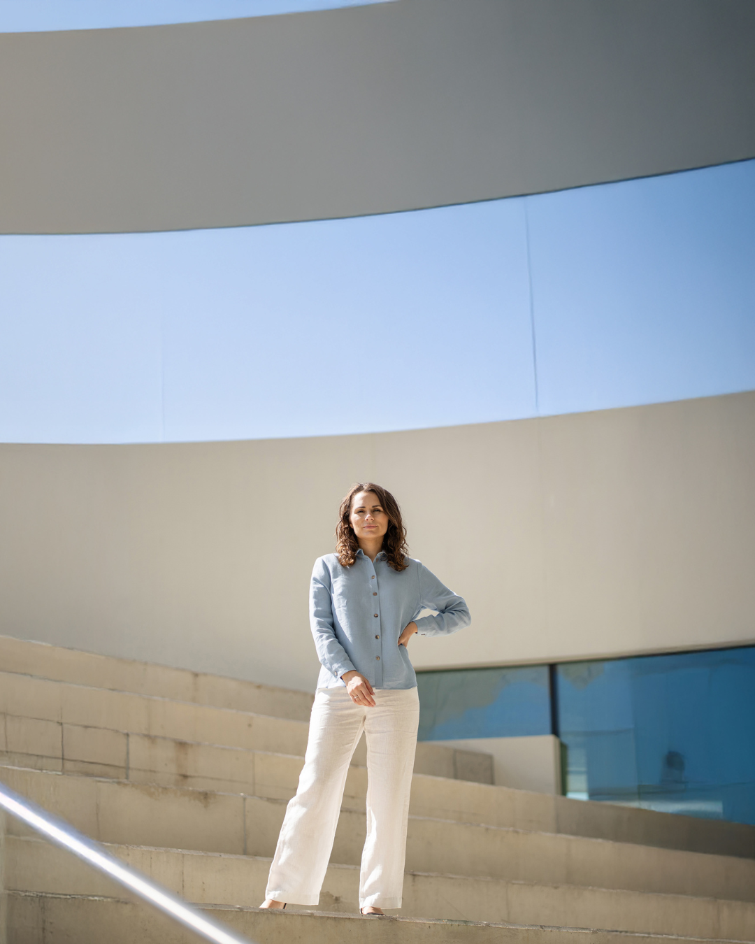 Vrouw staand op een moderne architectonische trap met een heldere blauwe lucht.