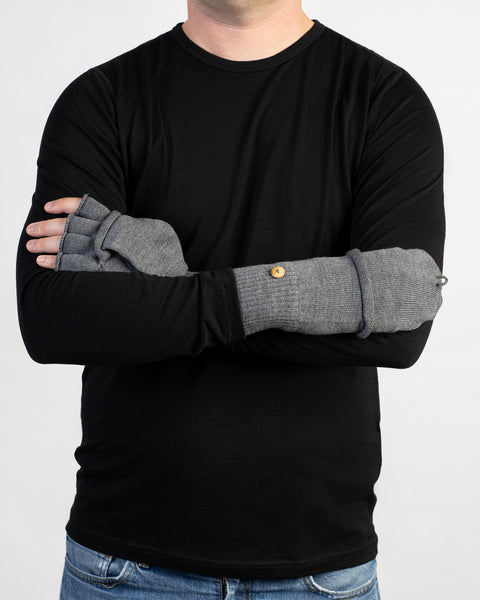 Man wearing gray convertible fingerless gloves with mitten flaps, arms crossed over a black shirt.