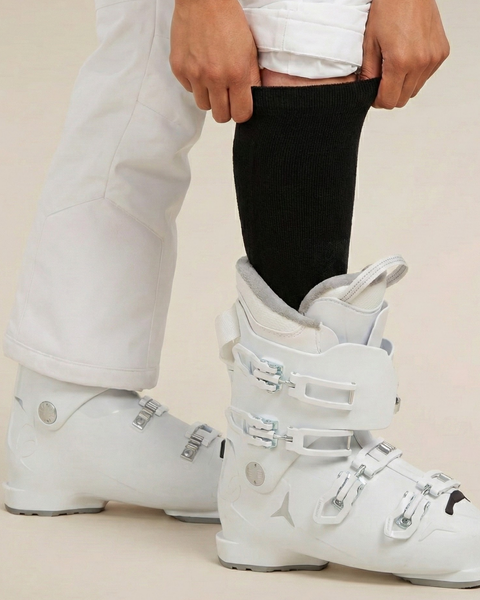 Close-up of black ski socks worn with white ski boots, showing snug fit and knee-high length for winter sports.