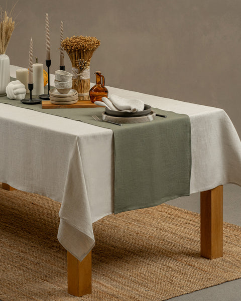Het menique linnen tafelkleed in puur witte kleur, dat over een houten tafel hangt, met een vaas en een set van een kleien beker en bord erop.