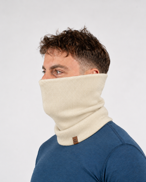 Man in a blue t-shirt wearing a beige neck gaiter pulled up over his nose and mouth.