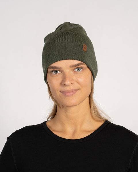 Woman wearing dark green knitted merino beanie with black top, studio background.