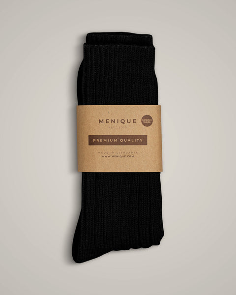 Black ribbed merino wool socks by Menique, folded neatly with a brown kraft paper label reading “Premium Quality – Made in Lithuania.” The thick knit socks are displayed on a light beige background, emphasizing their texture and quality.