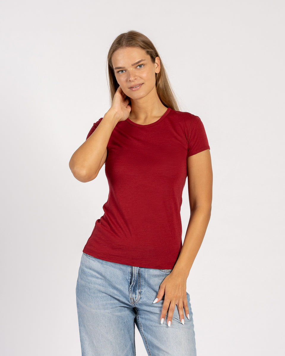 Vrouw draagt een Menique Royal Cherry t-shirt van merinowol en spijkerbroek, staand tegen een witte achtergrond.