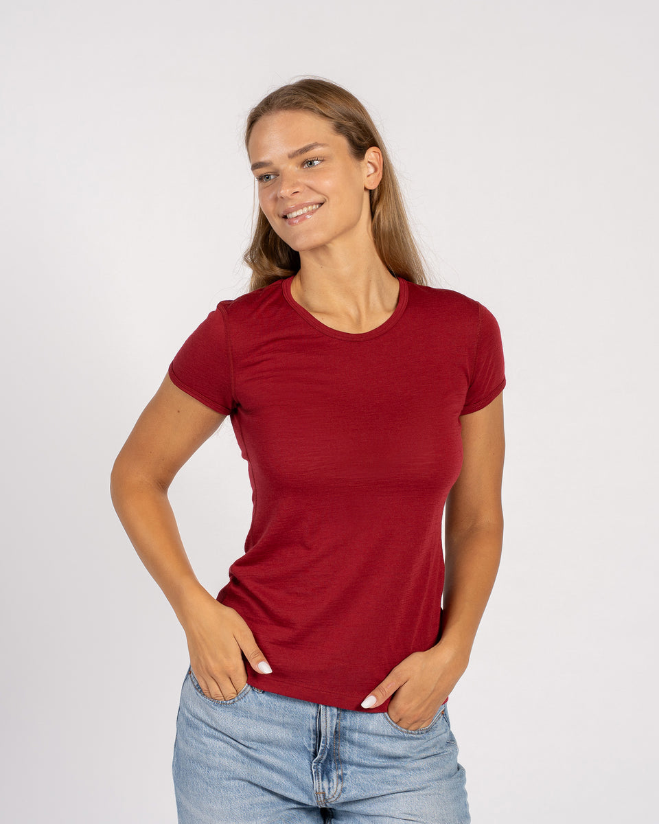 Vrouw draagt een Menique Royal Cherry t-shirt van merinowol en spijkerbroek, staand tegen een witte achtergrond.