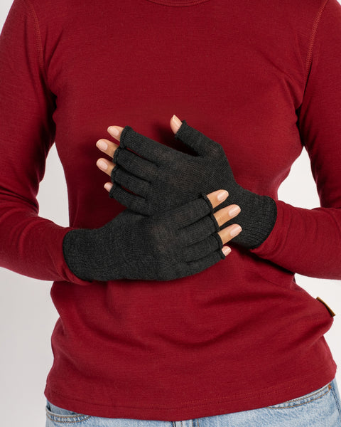 Close-up of a woman’s torso and hands wearing dark-gray fingerless merino gloves, palms crossed over her chest against a red top.