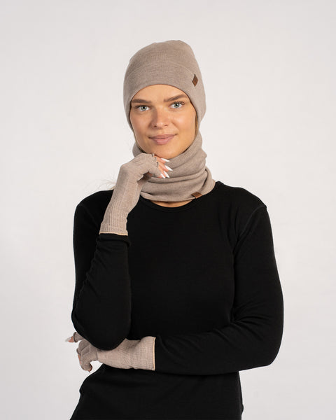 Woman wearing creamy beige knitted merino beanie, light neck gaiter and fingerless gloves with black top, studio background.