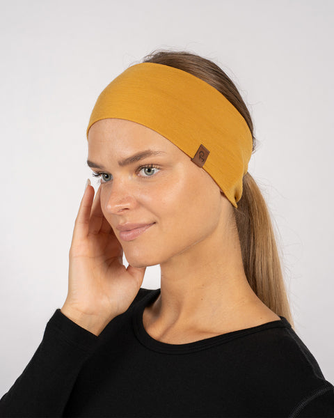 Close-up side view of woman in yellow merino headband, holding hand near face, wearing black shirt.