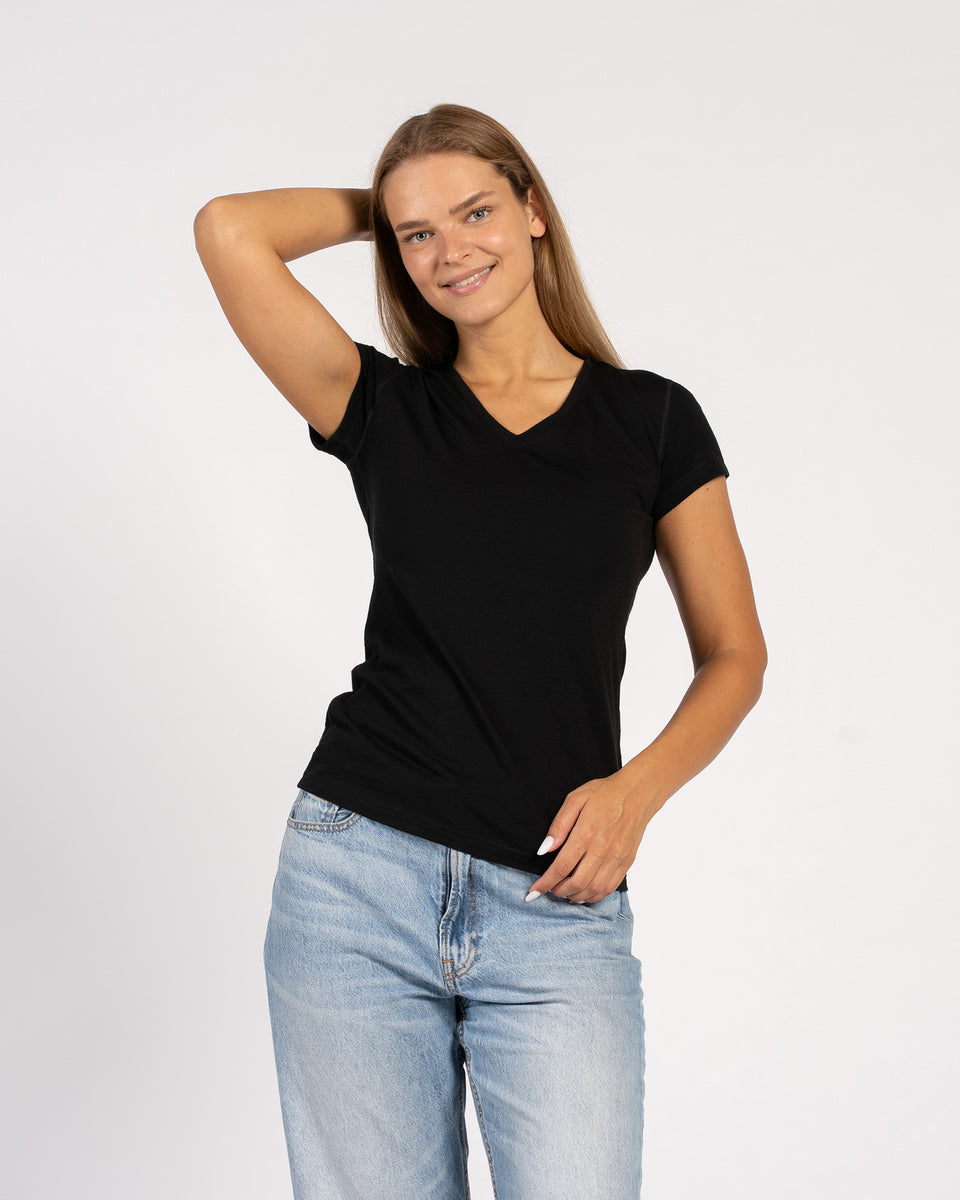 Vrouw poseert in een zwart T-shirt van merinowol met V-hals en korte mouwen.