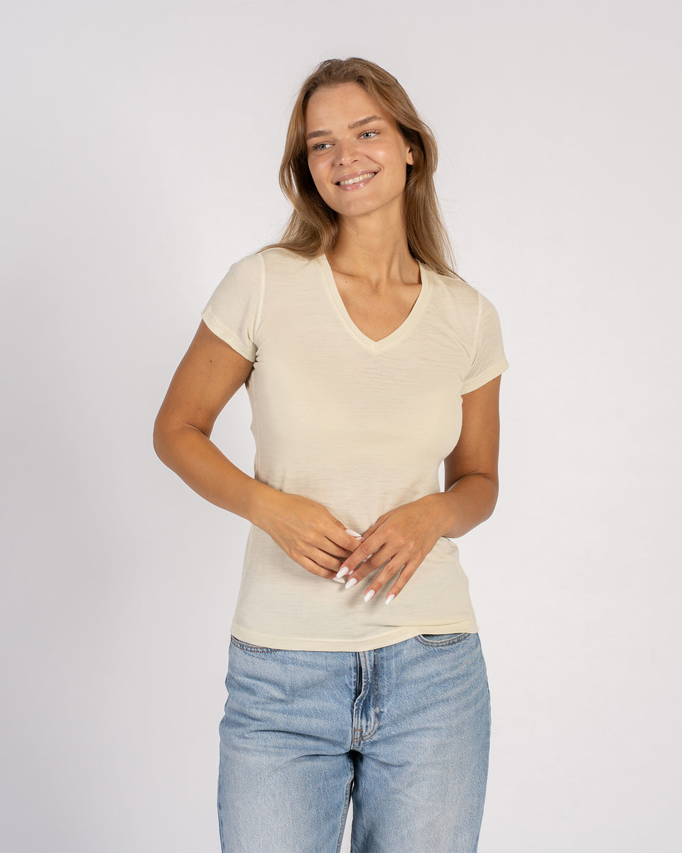 Vrouw draagt een T-shirt met V-hals van merinowol in natuurlijke kleur en korte mouwen.