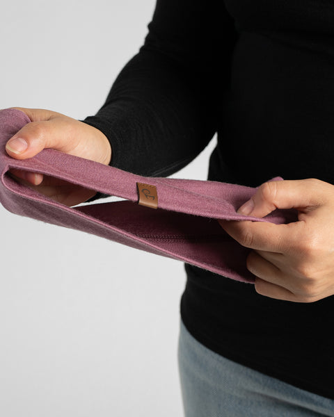 A close-up shot of hands holding and displaying a folded dusty rose or mauve knit headband.