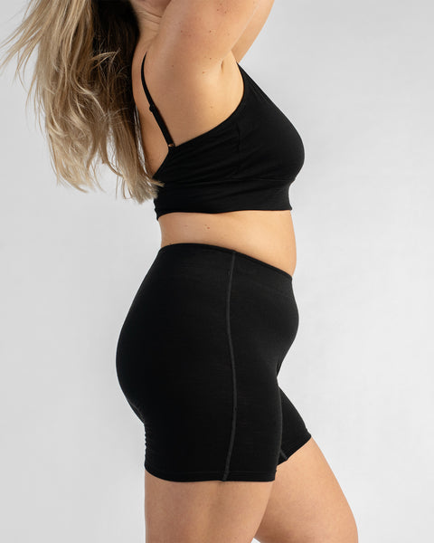 Side profile view of a model wearing a black sports bra with thin straps and black biker shorts.