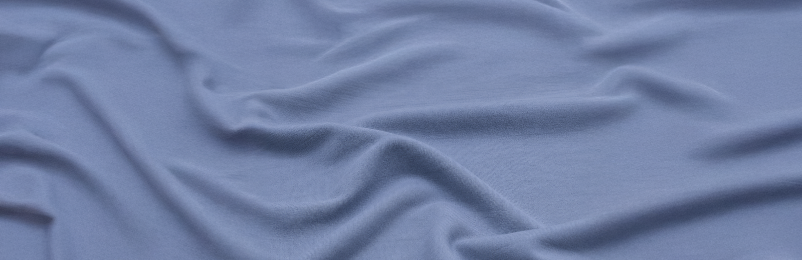 A close-up view of light periwinkle-blue fabric, gently gathered to highlight its soft texture and subtle draping.